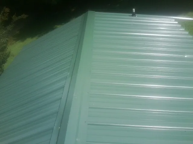 New green metal panels meeting at the ridge of a roof — Flat Roof Repair work by our crew in Wonder Lake