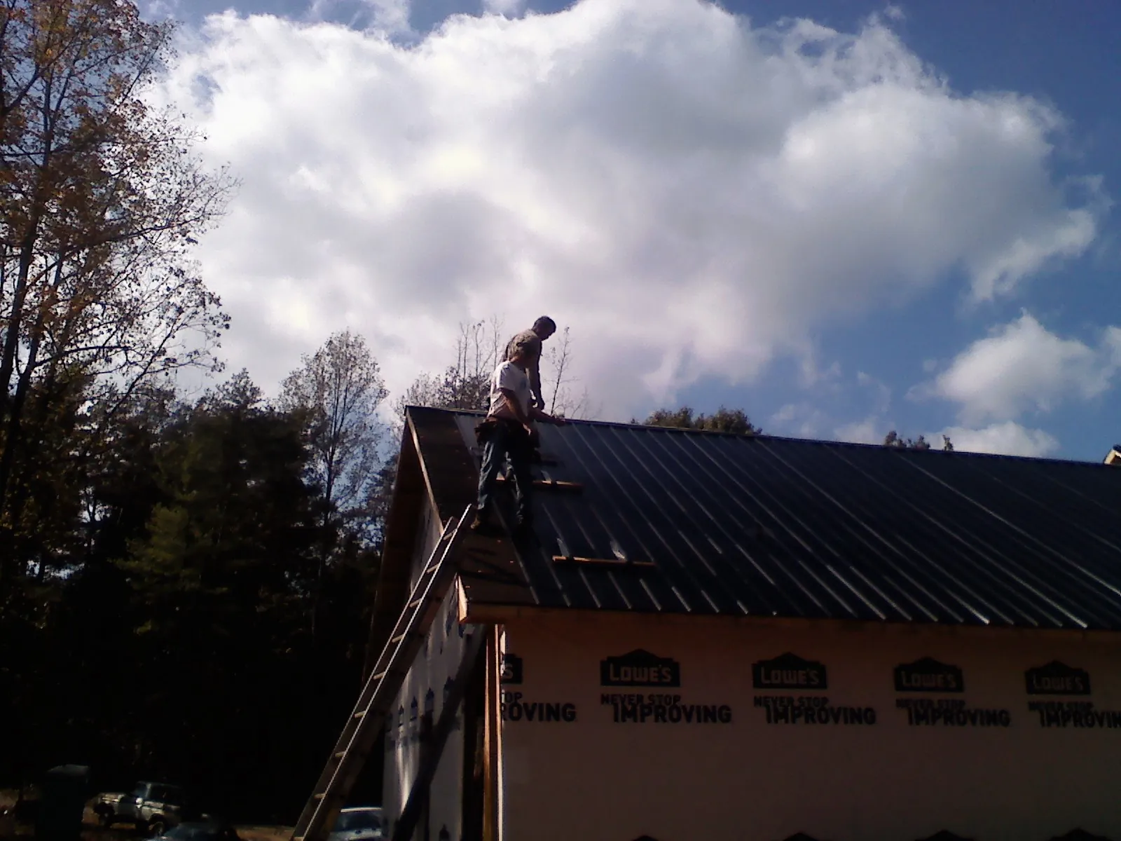 Roofer fastening dark metal panels high against a cloudy sky, from a Roof Inspection job in Wonder Lake