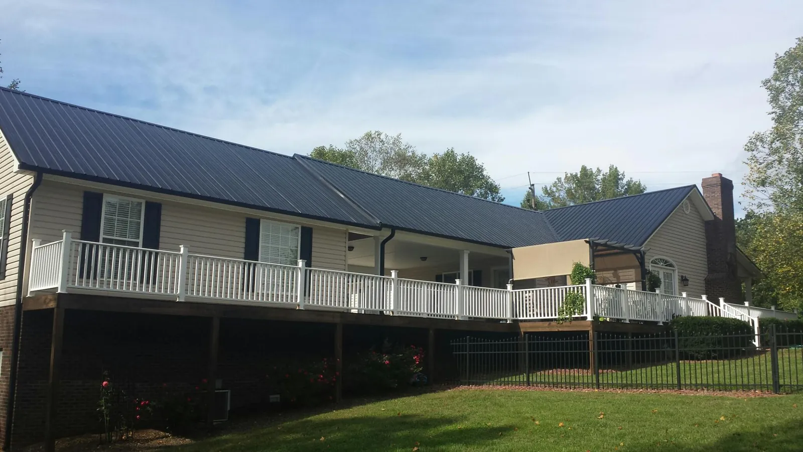 Black metal roof above a long white railed deck on a hillside home in Wonder Lake