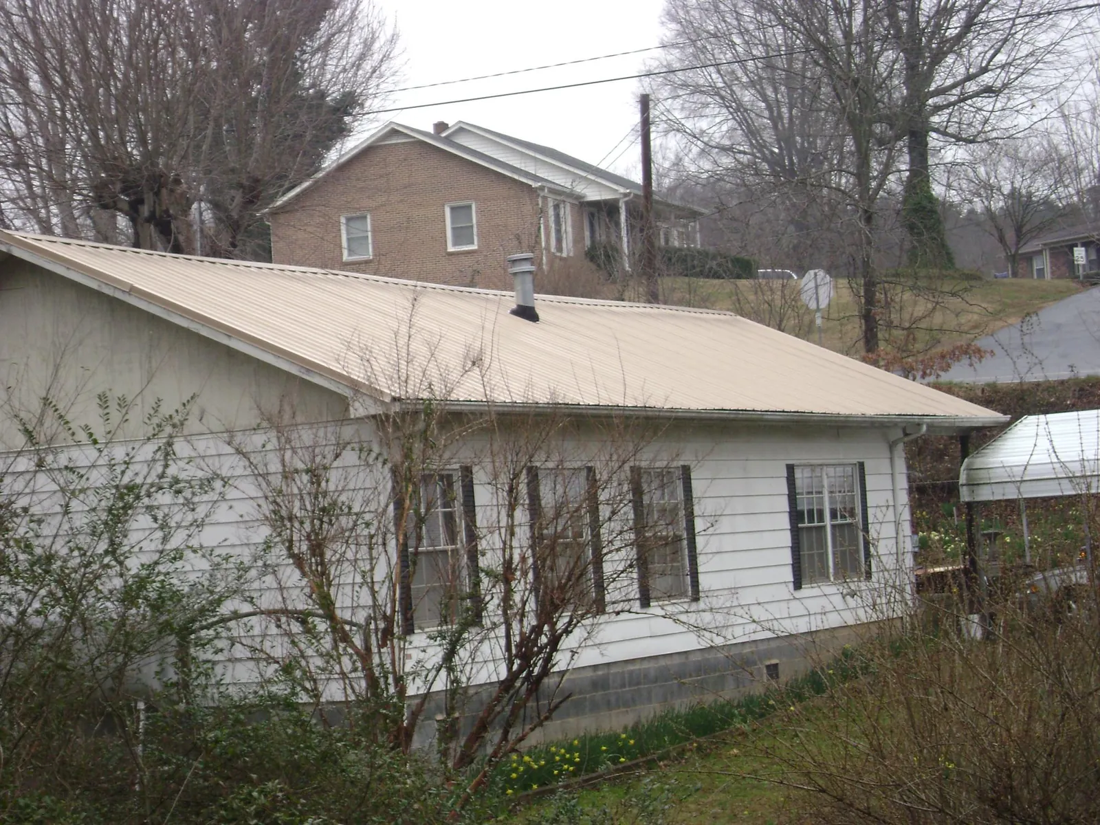 Tan metal roof on a white sided house set into a hillside — Commercial Roofing by Roofing Brothers in Wonder Lake
