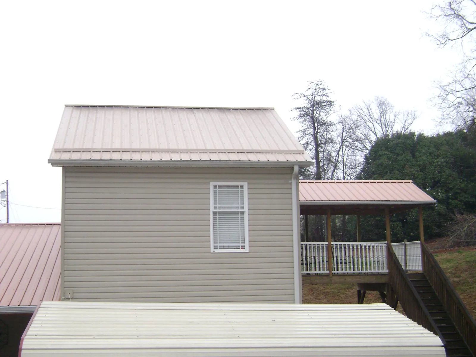 Tan metal roofs on a two story addition and attached porch, from a Roof Replacement job in Wonder Lake